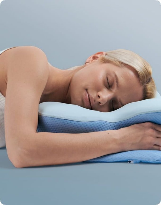 A woman sleeping on her side, her head and neck gently cradled in the contour of the blue Derila Ergo pillow.